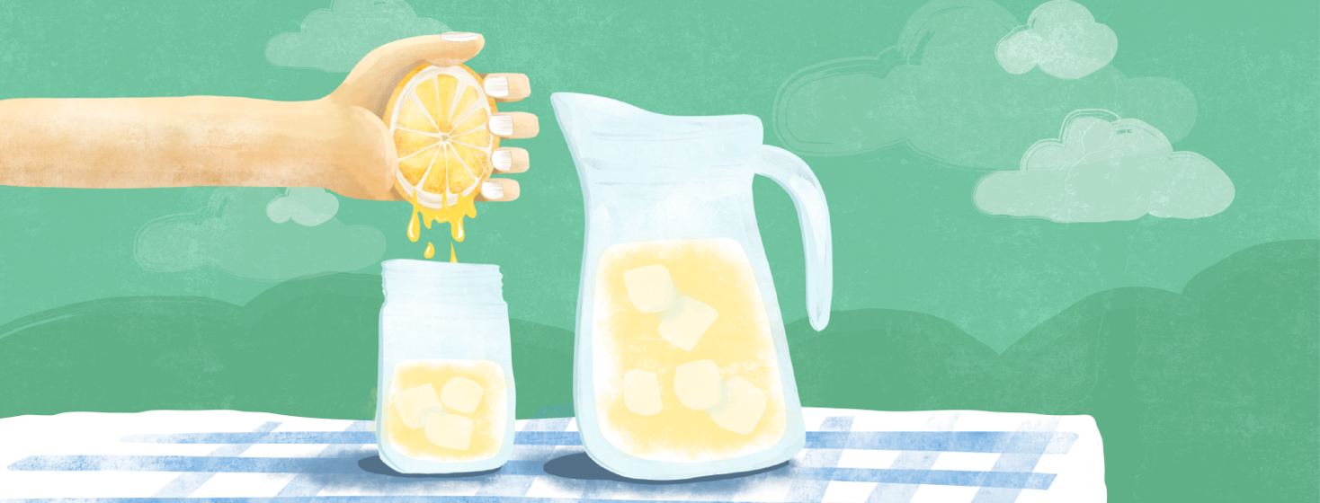 A hand squeezing a lemon into glass of lemonade